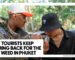 WHY TOURISTS KEEP COMING BACK FOR THE BEST WEED IN PHUKET - Two young men standing outdoors in a lush environment, with one holding a clear glass jar of cannabis while the other leans in to smell it.